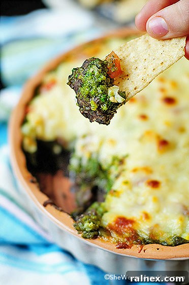Delicious Warm Layered Black Bean Dip topped with cilantro pesto and melted cheese, ready to be served at a party.